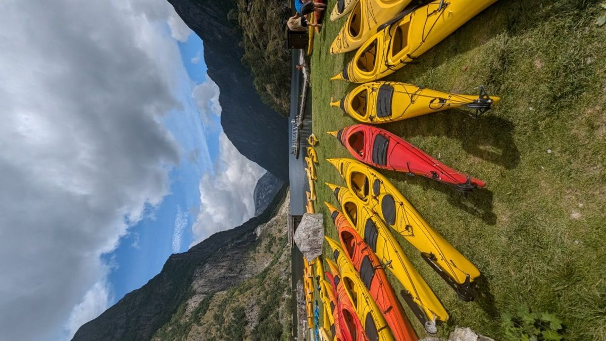 Colorful kayaks lined up by the fjord with mountains in the background